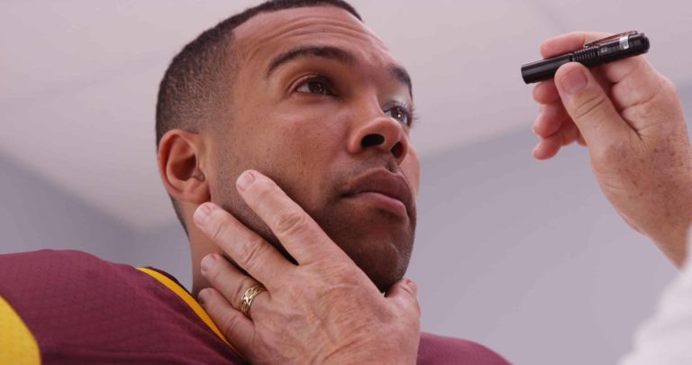 Mid aged doctor checking football player's eyes with flashlight